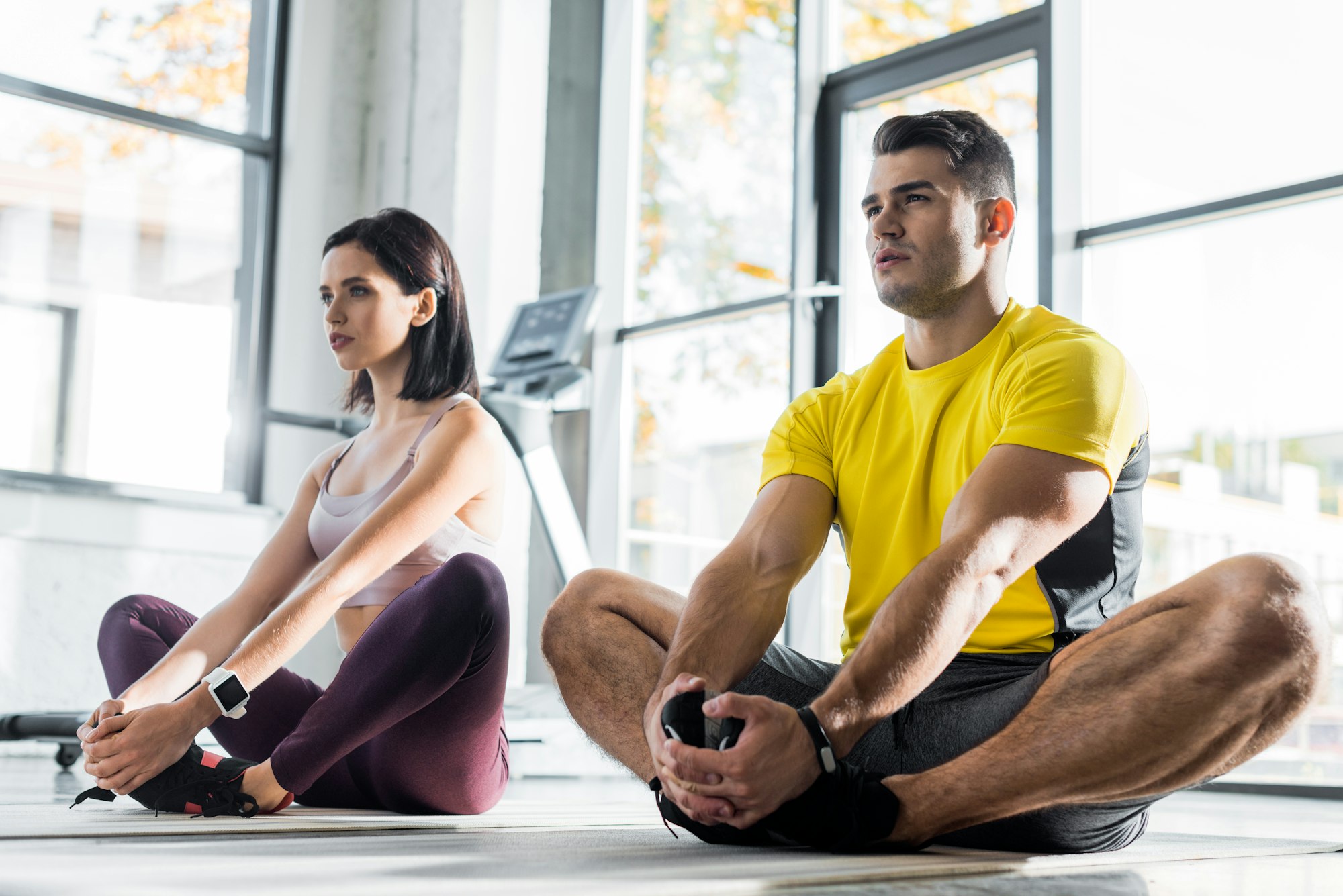 sportsman and sportswoman stretching on fitness mats in sports center