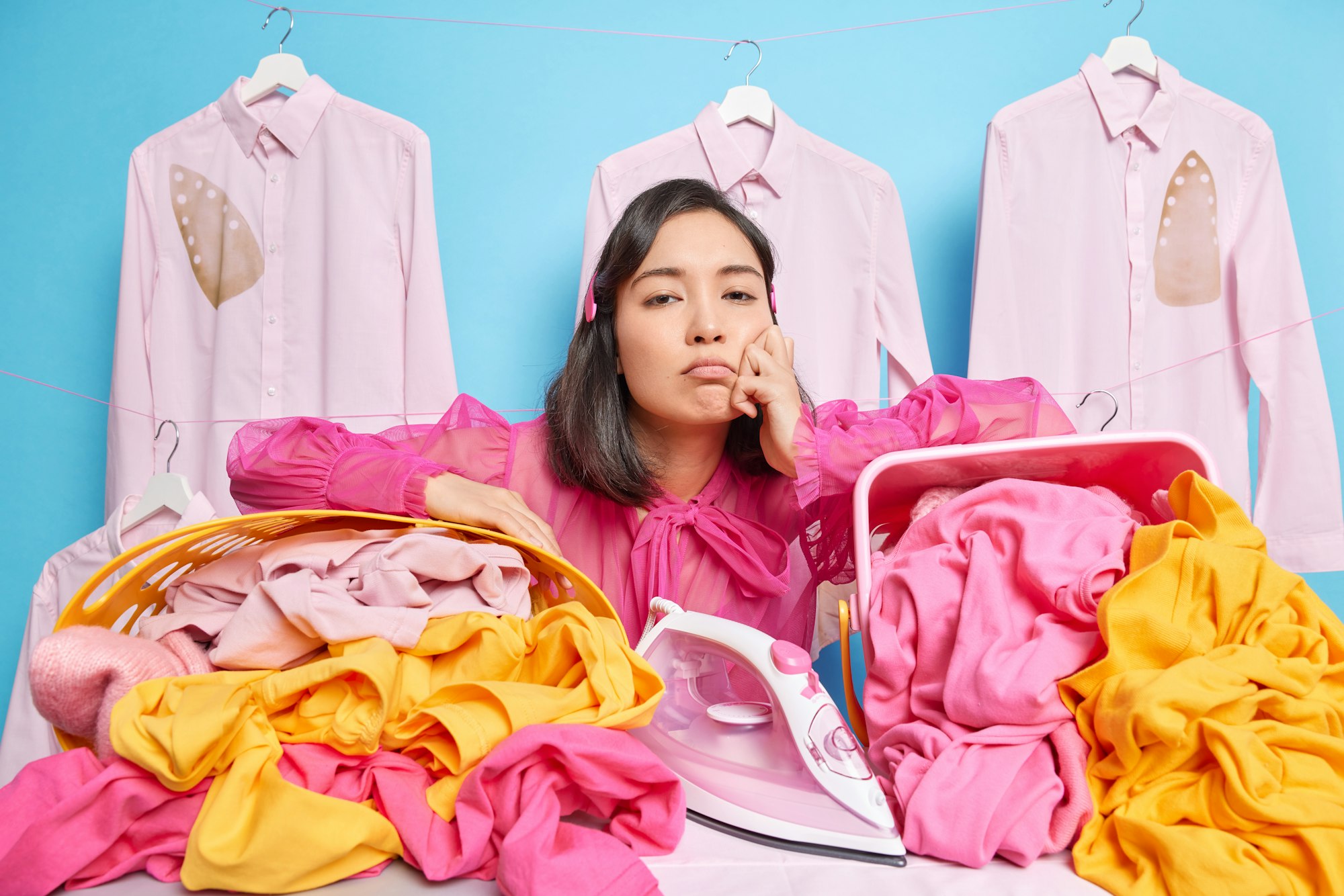 Upset laundry worker leans at baskets full of linen feels tired busy ironing poses against blue back