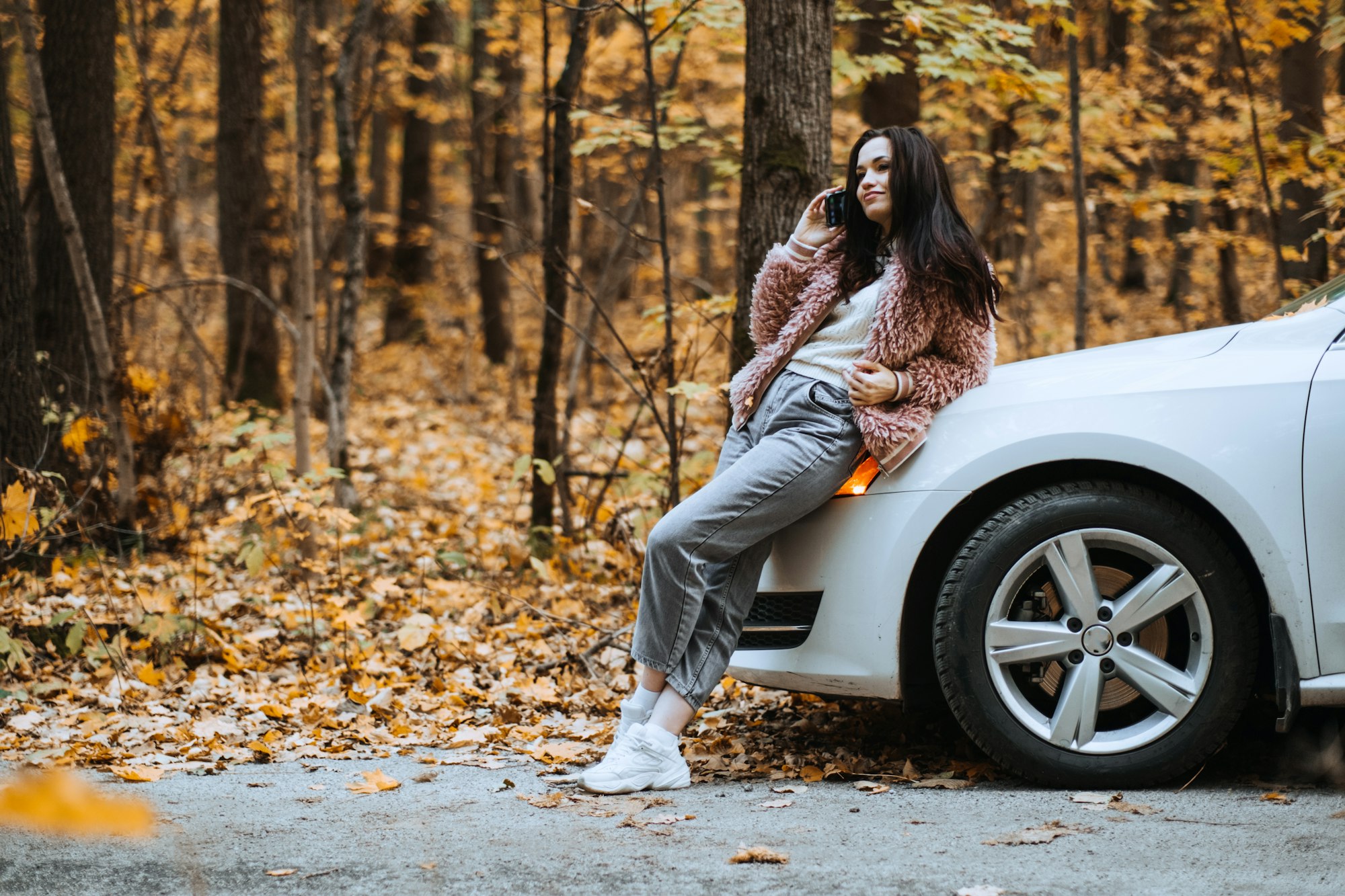 Confident brunette woman standing near car and call phone. Preparing Your Car For Fall autumn