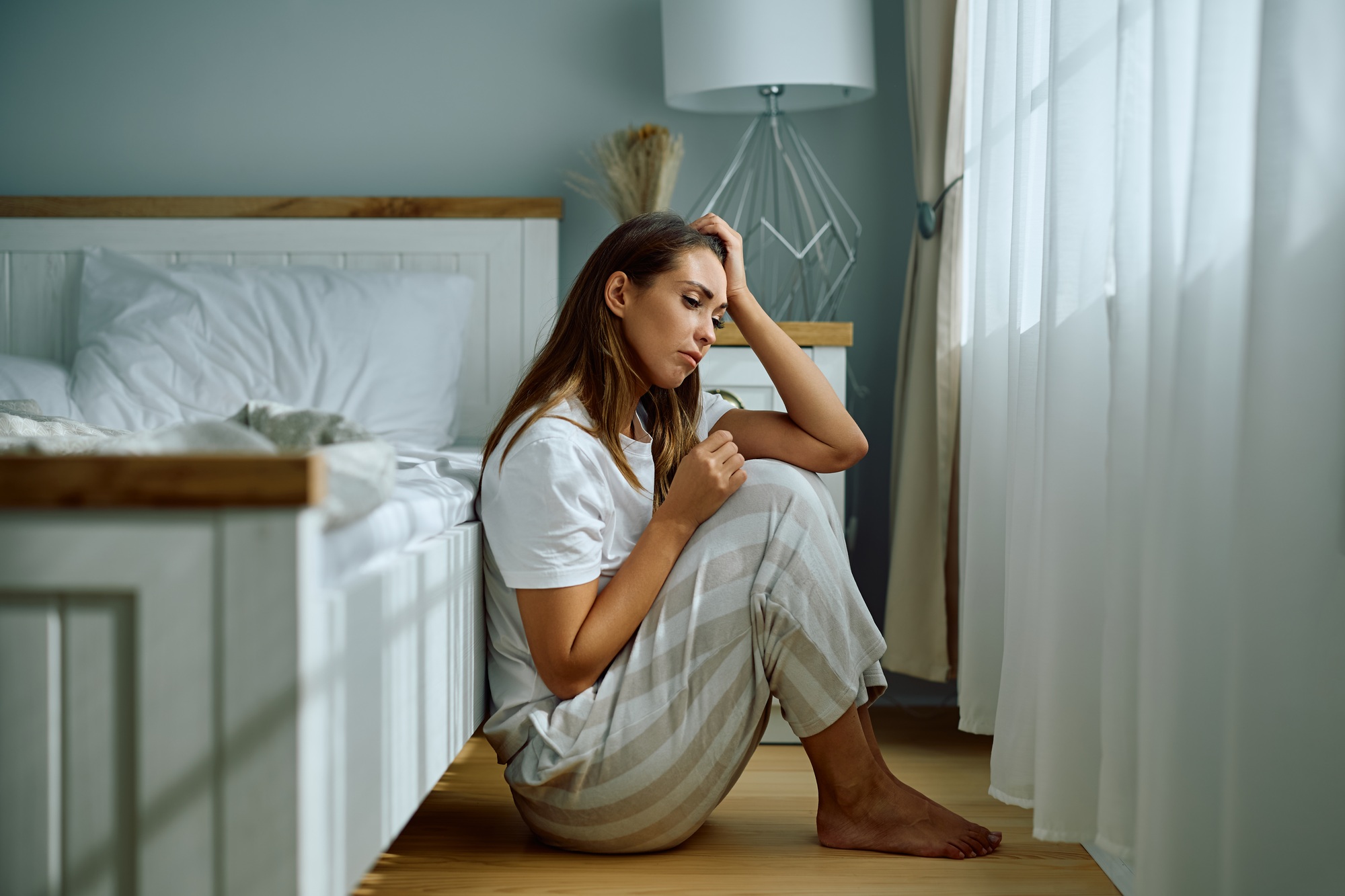 Young stressed woman sitting on the floor in bedroom.